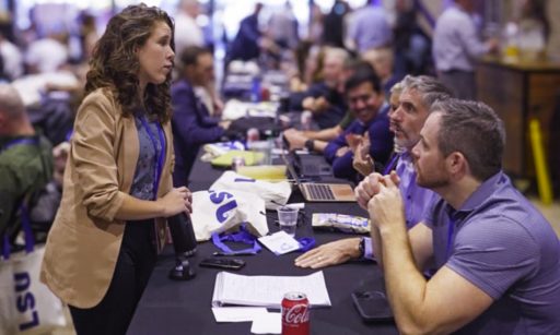 LeadSimple team at an event sitting at a long table, speaking to a woman about operations management software