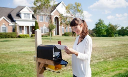 A smiling woman collects direct mail advertising from her mailbox outside her home