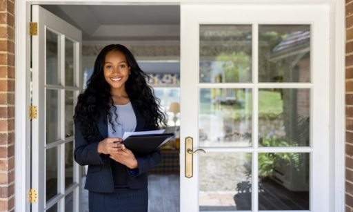 A smiling property manager emerges from a house with documents