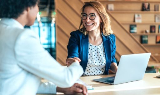 a woman smiling and shaking hands with a client after closing the deal