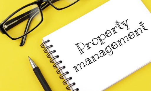 A pair of glasses, pen, and a property management notebook lie on a yellow table.