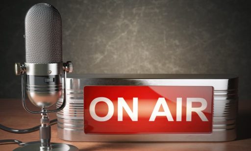 A vintage microphone on a table beside a studio “On Air” sign.