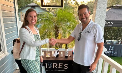 Patrick Arenson stands on the back porch of a house in front of an LRES Property Management booth shaking the hands of an event patron.