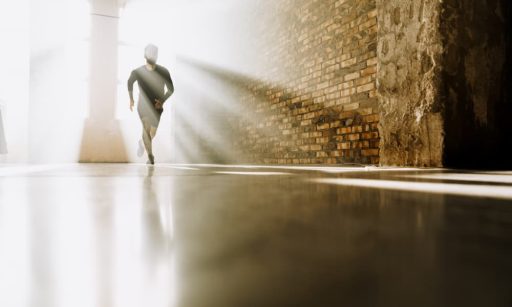 A man running forward through a corridor, backlit by sunshine.